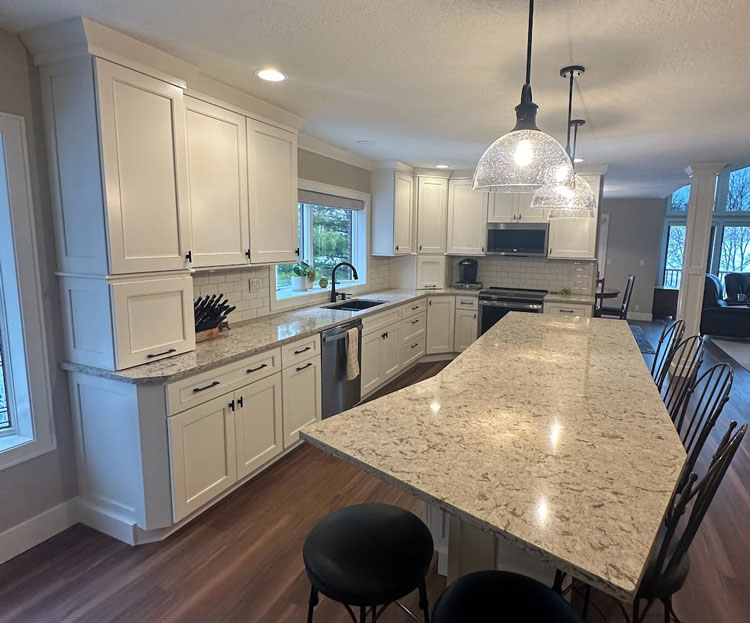 Kitchen remodel with new white cabinets and quartz countertop and a kitchen island with barstool seating space.