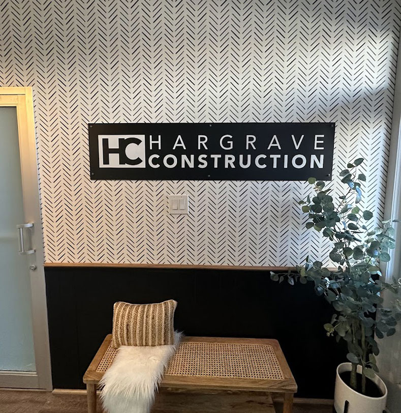 Hargrave Construction logo hanging on the wall of their building with a herringbone black and white patterned wallpaper.