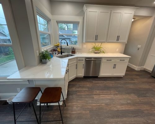 Kitchen remodel showing new white cabinets and white quartz countertop with a corner sink. The cabinet wraps around the wall with space for two barstools.