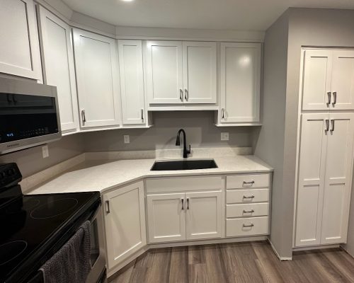 Kitchen remodel showing new white countertops, black seek, and a built-in pantry area.