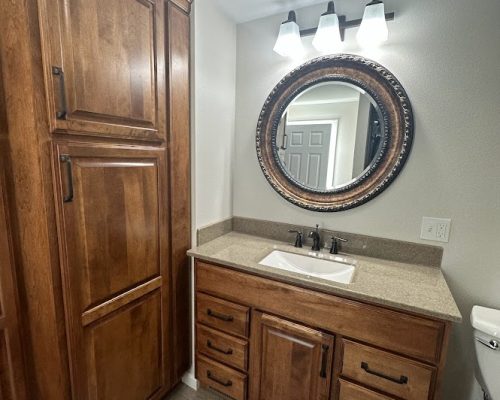 Bathroom remodel showing new cabinets under the sink with new quartz countertop and a large, circular mirror.