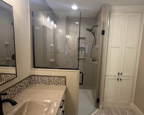 Bathroom remodel with a large shower custom-built to fit in the corner and extend outwards with floor-to-ceiling cabinets next to it.